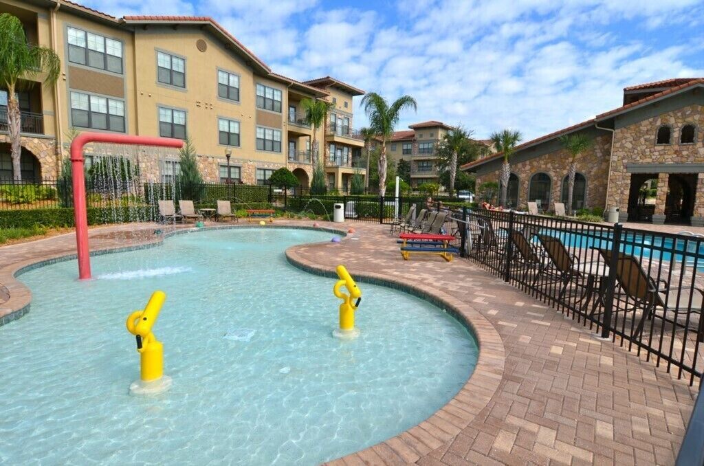 A pool area with two yellow water features, a brick walkway, and a building with multiple balconies.
