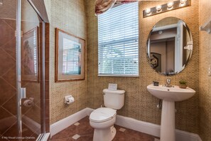 Un baño con cabina de ducha de vidrio, inodoro, lavabo y ventana con persianas.