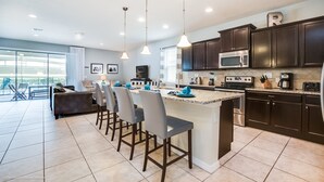 A modern kitchen with dark cabinets, a large island with bar stools, a microwave, and a coffee maker. - 8 Bed Villa with Games, Pool & Spa (Kissimmee)