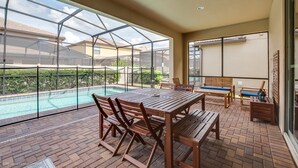 A covered patio with a pool, wooden furniture, and a view of neighboring houses. - 8 Bed Villa with Games, Pool & Spa (Kissimmee)