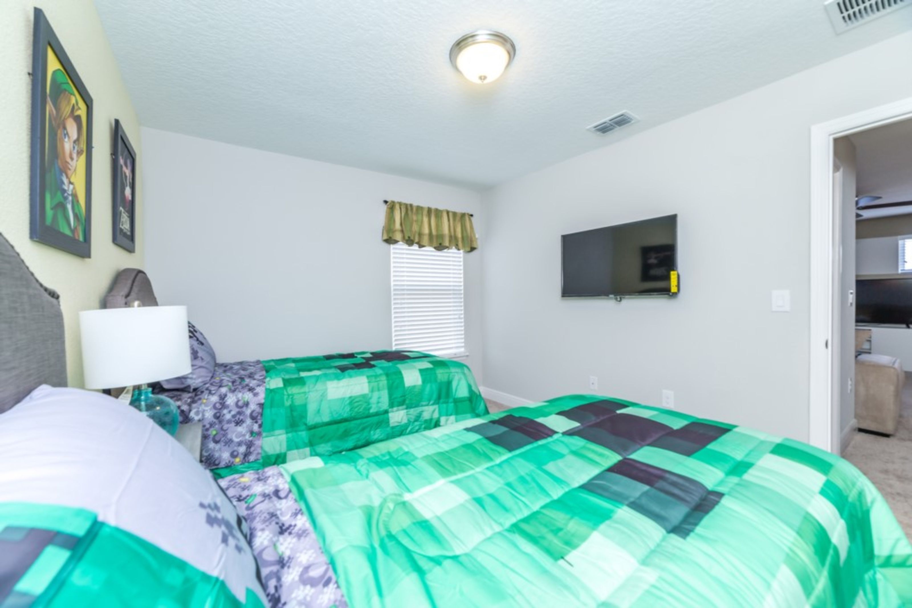 A bedroom with two beds, a television on the wall, and a window with blinds.
