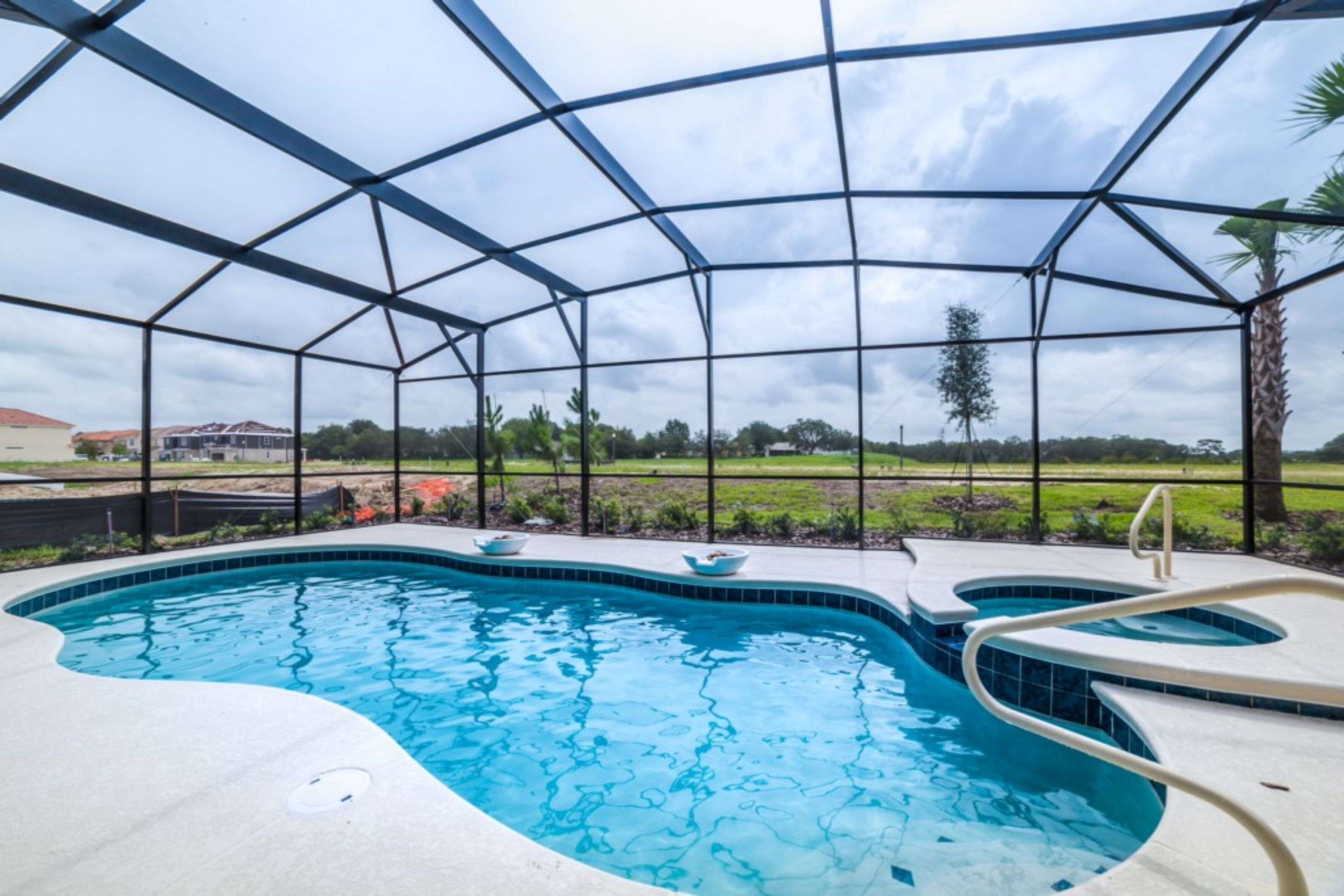 Una piscina con borde curvo, rodeada por una zona cubierta con estructura metálica y paneles de vidrio.