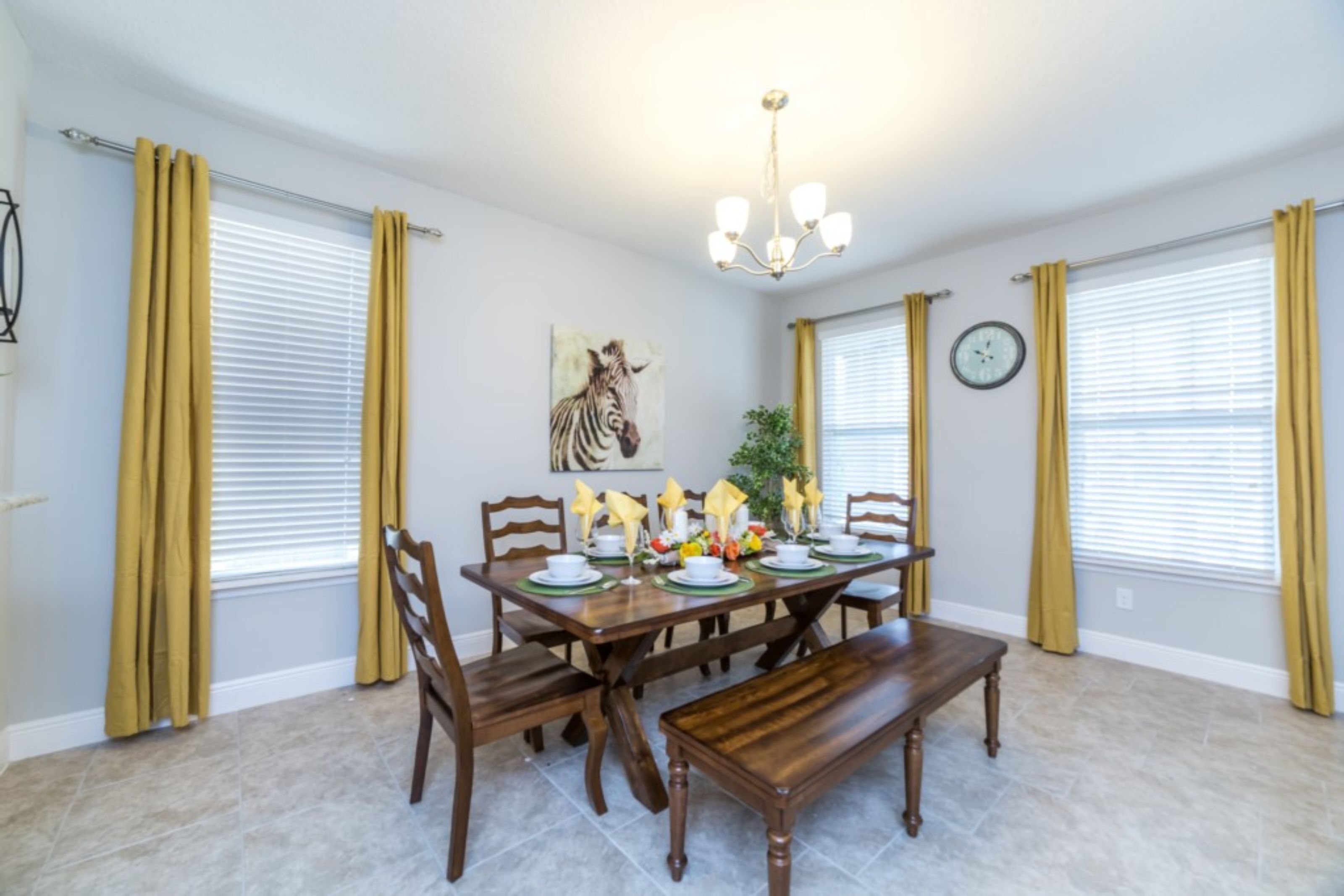 A dining room with a wooden table set for four, surrounded by chairs, a bench, and a chandelier.
