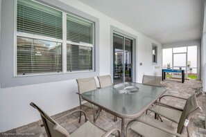 Un espace patio avec une table et des chaises à plateau en verre, une table de billard et une vue sur la rue.