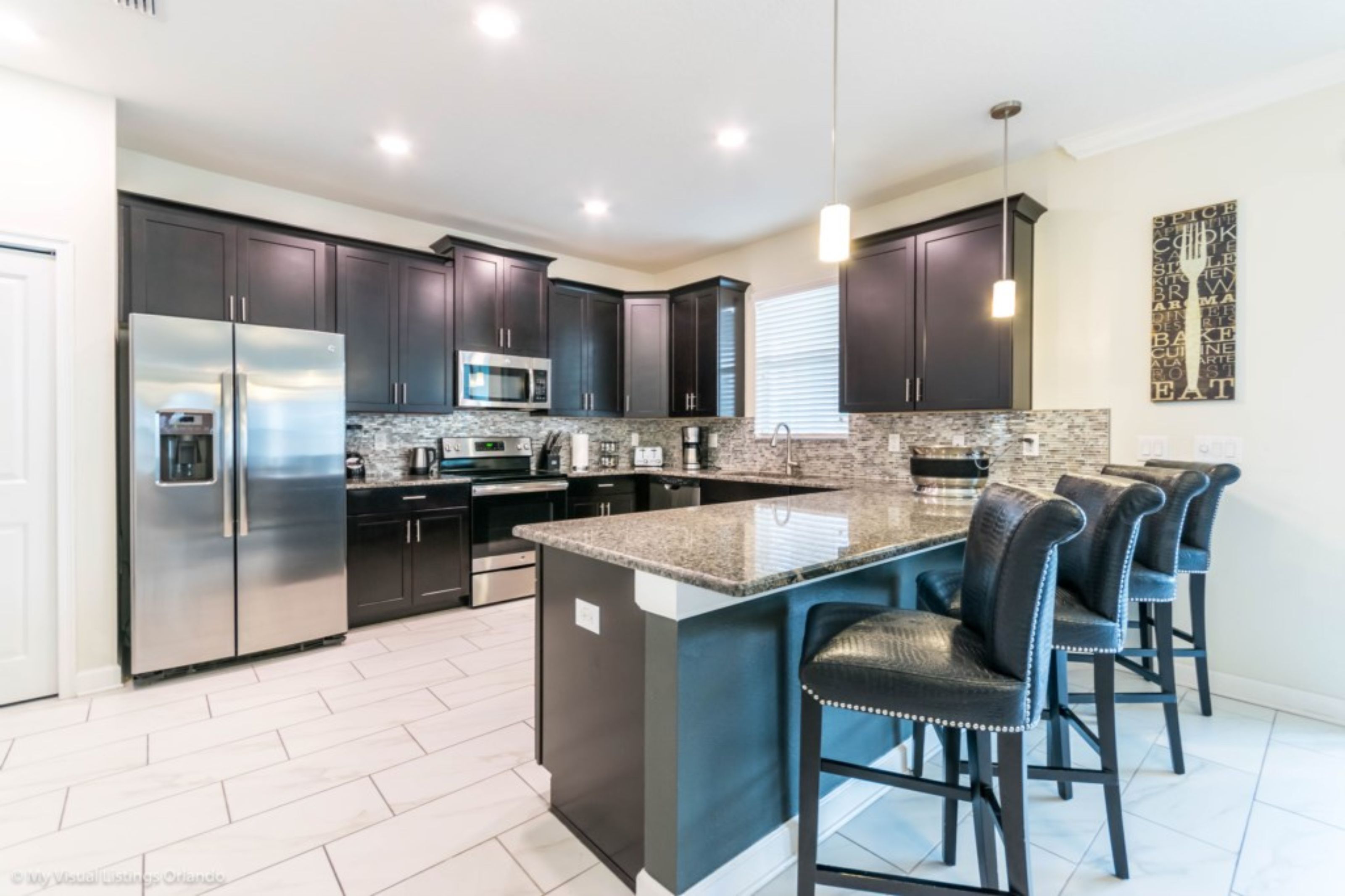 A modern kitchen with dark cabinets, stainless steel appliances, a granite island, and bar stools.