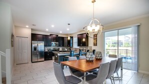 A modern kitchen with dark cabinets, stainless steel appliances, and a dining area with a wooden table and grey chairs. - 6 Bedroom Resort Villa With Spa (Davenport)