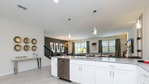 A modern kitchen with white cabinetry, a stainless steel dishwasher, and pendant lighting. - 9 Bedroom Champions Gate Villa (Kissimmee)