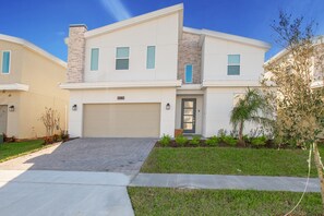 A two-story residential building with a garage, a front entrance with a door, and a small front yard with grass and plants.