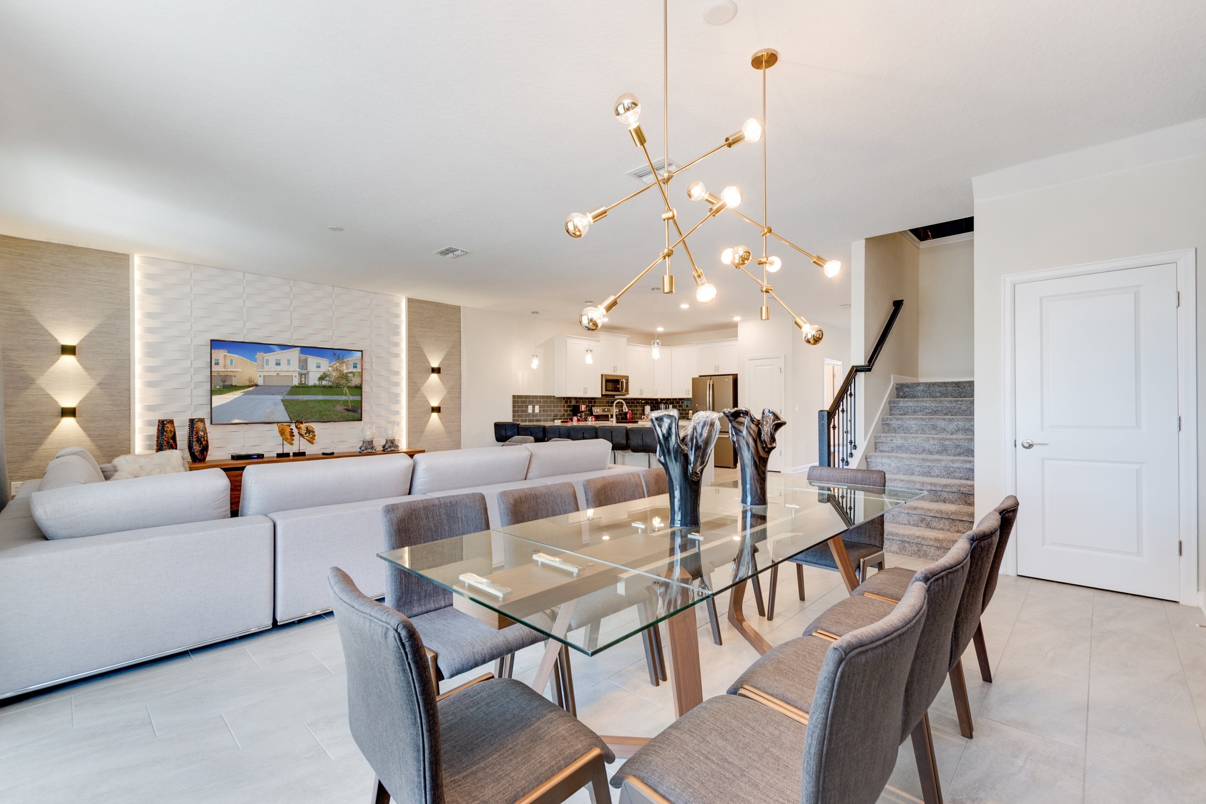 A modern living room with a glass dining table, grey sofas, and a contemporary chandelier.