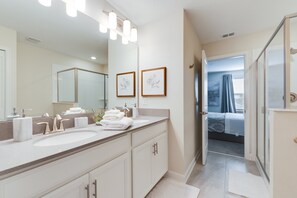 A modern bathroom with dual sinks, a large mirror, and a shower area.