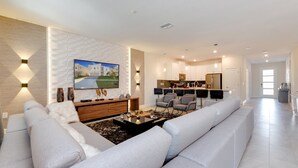 A modern living room with a large sectional sofa, a coffee table, and a TV mounted on the wall. - 9 Bedroom Champions Gate Villa (Kissimmee)