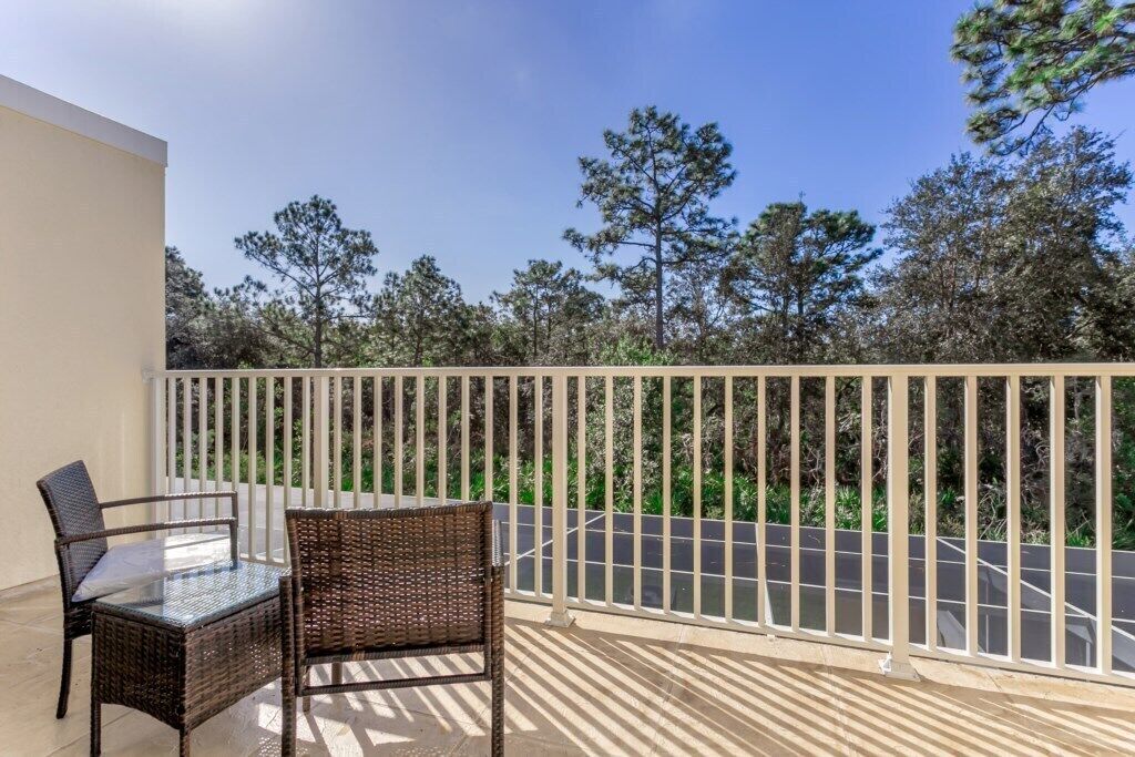 A balcony with wicker furniture and a view of trees and a road.