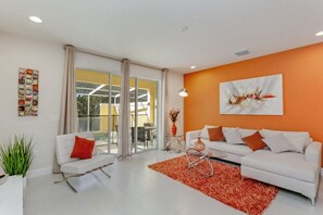 A modern living room with a white sofa, red rug, and a large window with a view of a yellow building.