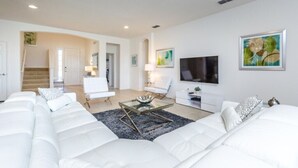 A modern living room with a large white sofa, a glass coffee table, and a flat-screen TV mounted on the wall. - Cool and Modern 9 Bed 7 Ba Villa Pool & Spa 6160boa (Davenport)