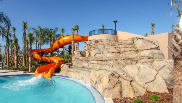 A water park with a large water slide, a pool, and palm trees. - Elegant 5 Bed 4,5 Ba Villa Game Room Pool Spa 5298w (Davenport)