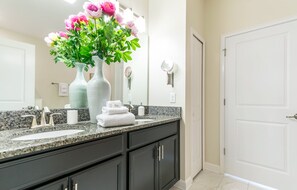 A bathroom with a granite countertop, two sinks, a large mirror, and a vase with flowers. - 9085hs (Davenport)