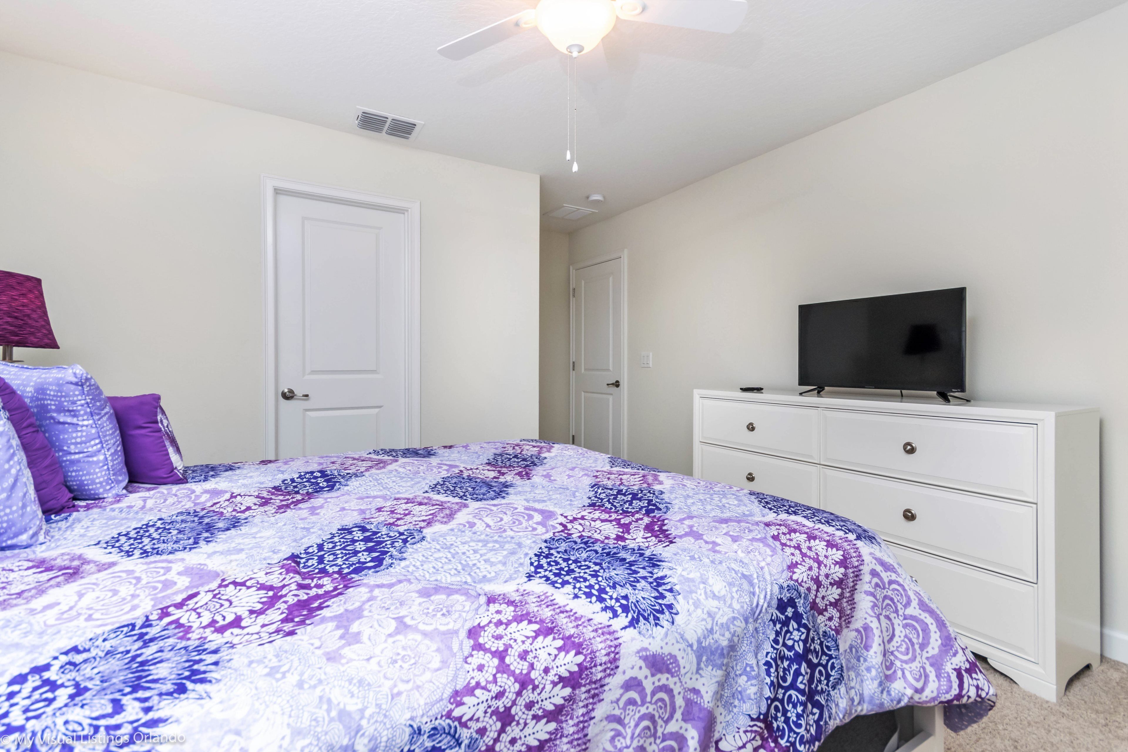 A bedroom with a bed, a dresser, a television, and a ceiling fan.