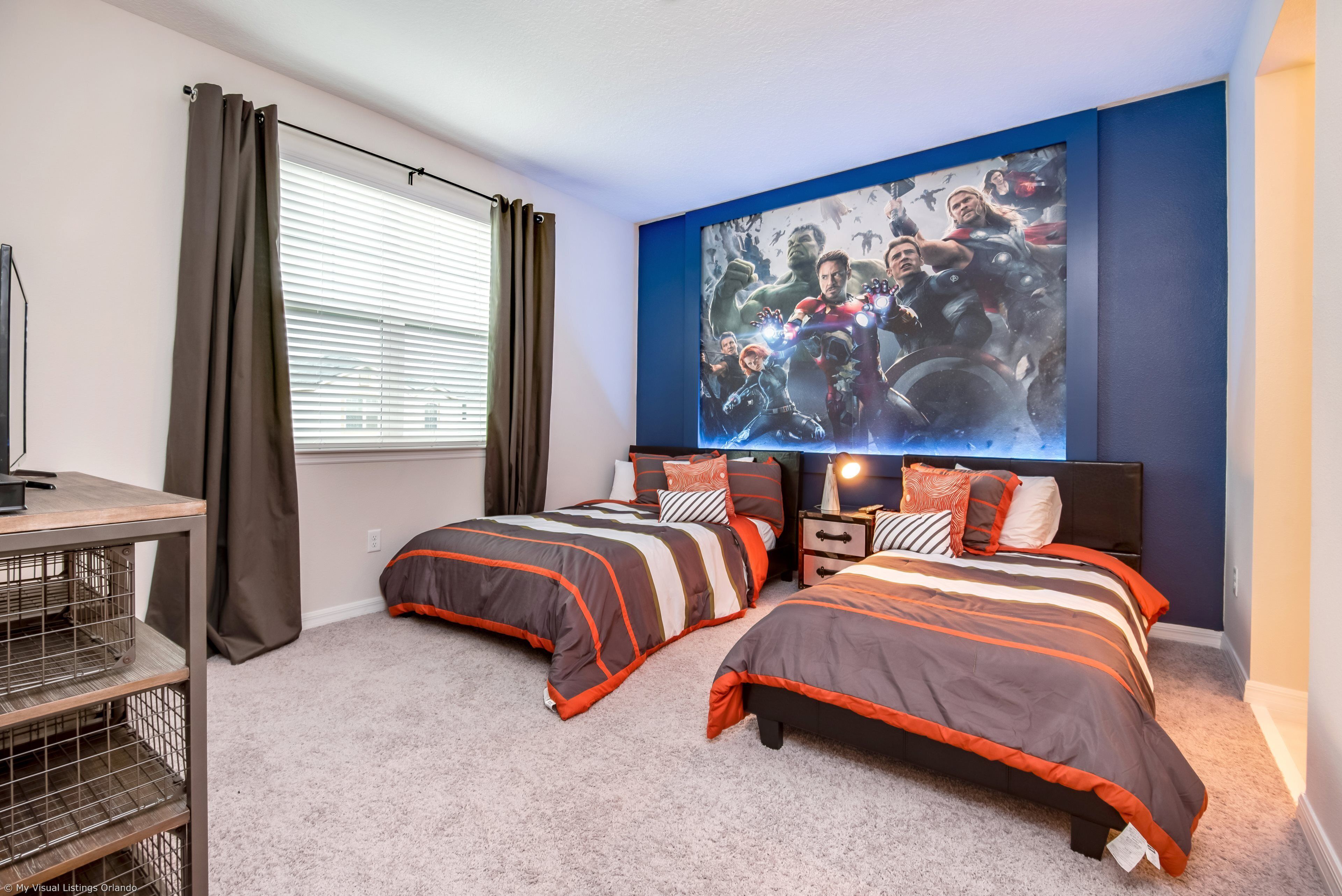 A bedroom with two beds, a large poster on the wall, a desk, and a window with curtains.