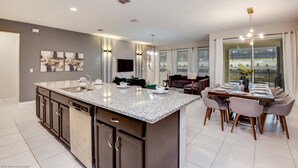 A modern kitchen with granite countertops, stainless steel appliances, and a dining area with a large table and chairs. - 1780spp New 7 Bedroom 5 Bathroom Solara Villa (Kissimmee)