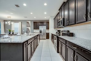 A modern kitchen with dark wooden cabinets, stainless steel appliances, and a granite countertop. - 1780spp New 7 Bedroom 5 Bathroom Solara Villa (Kissimmee)