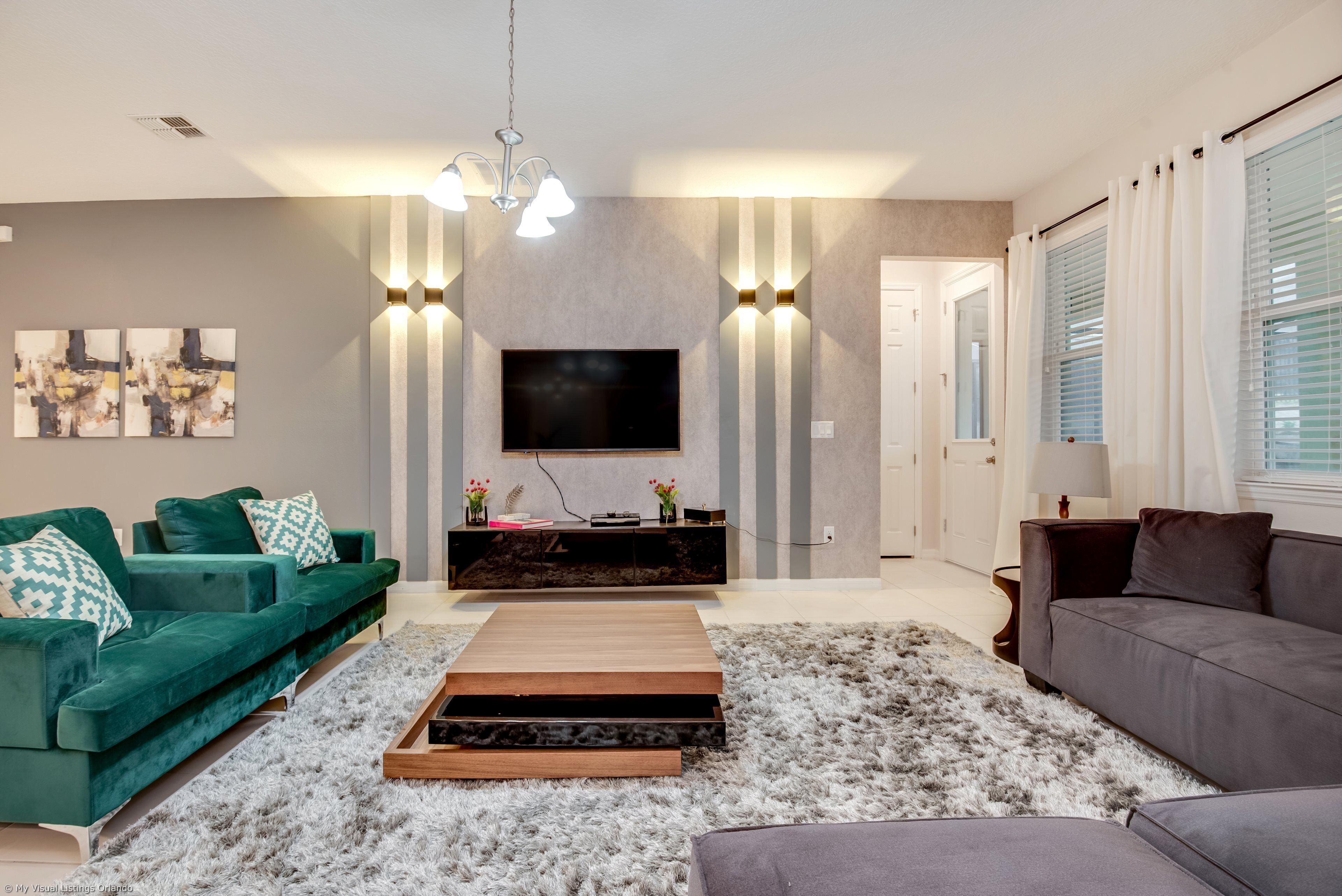 A modern living room with a green sofa, a grey sofa, a wooden coffee table, and a flat-screen TV mounted on the wall.
