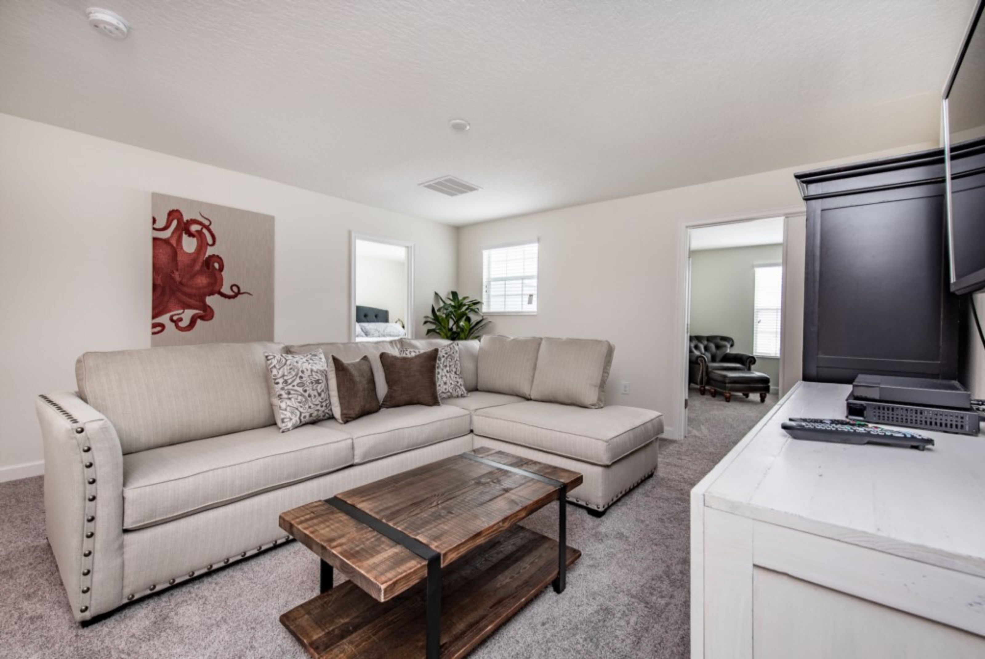 A living room with a sectional sofa, a coffee table, a TV, and a large painting on the wall.