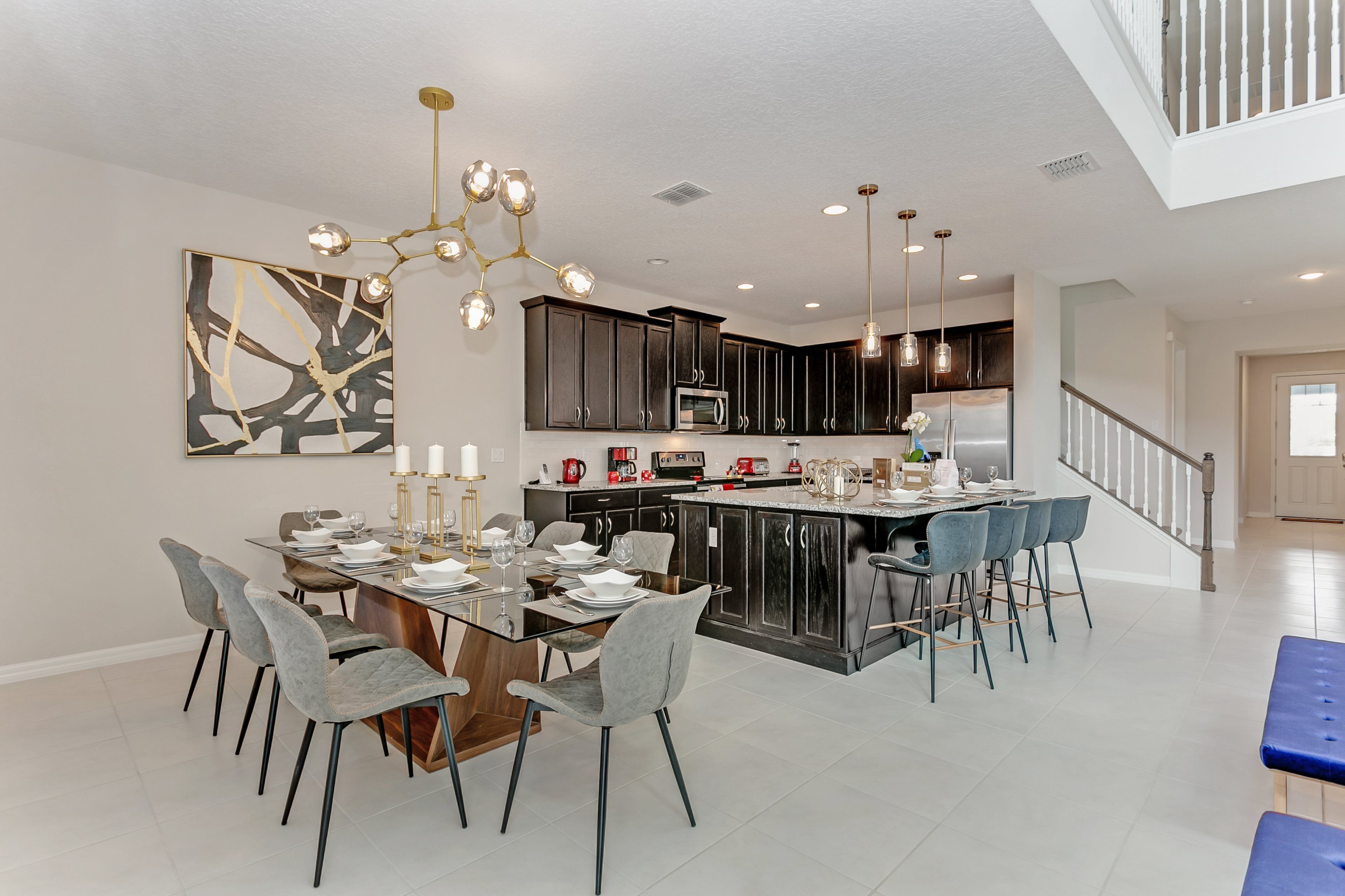 A modern kitchen with dark cabinets, a central island, and a dining area with a glass table and grey chairs.