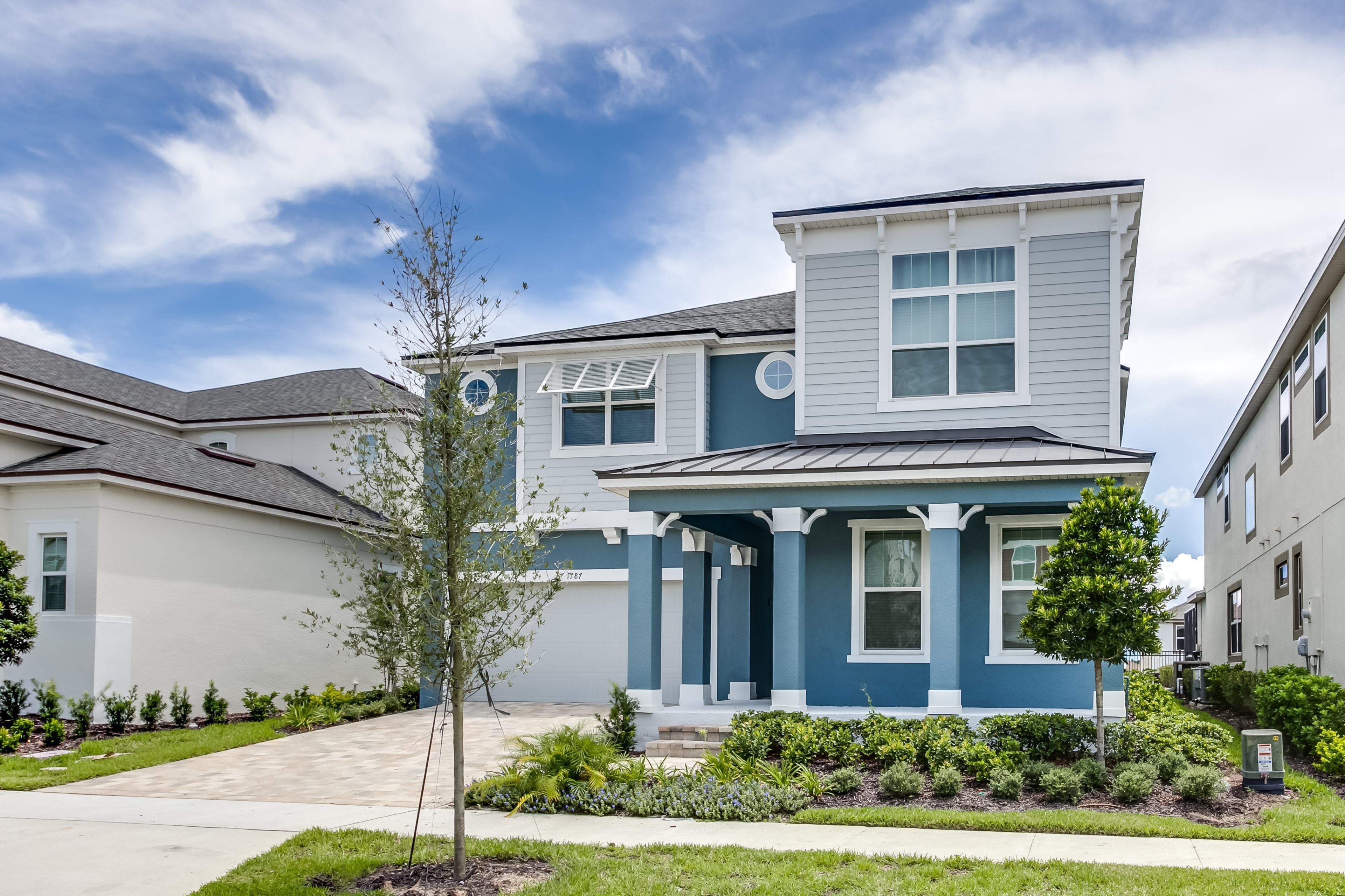 A two-story residential building with a blue and white exterior, a covered front porch, and a landscaped front yard.