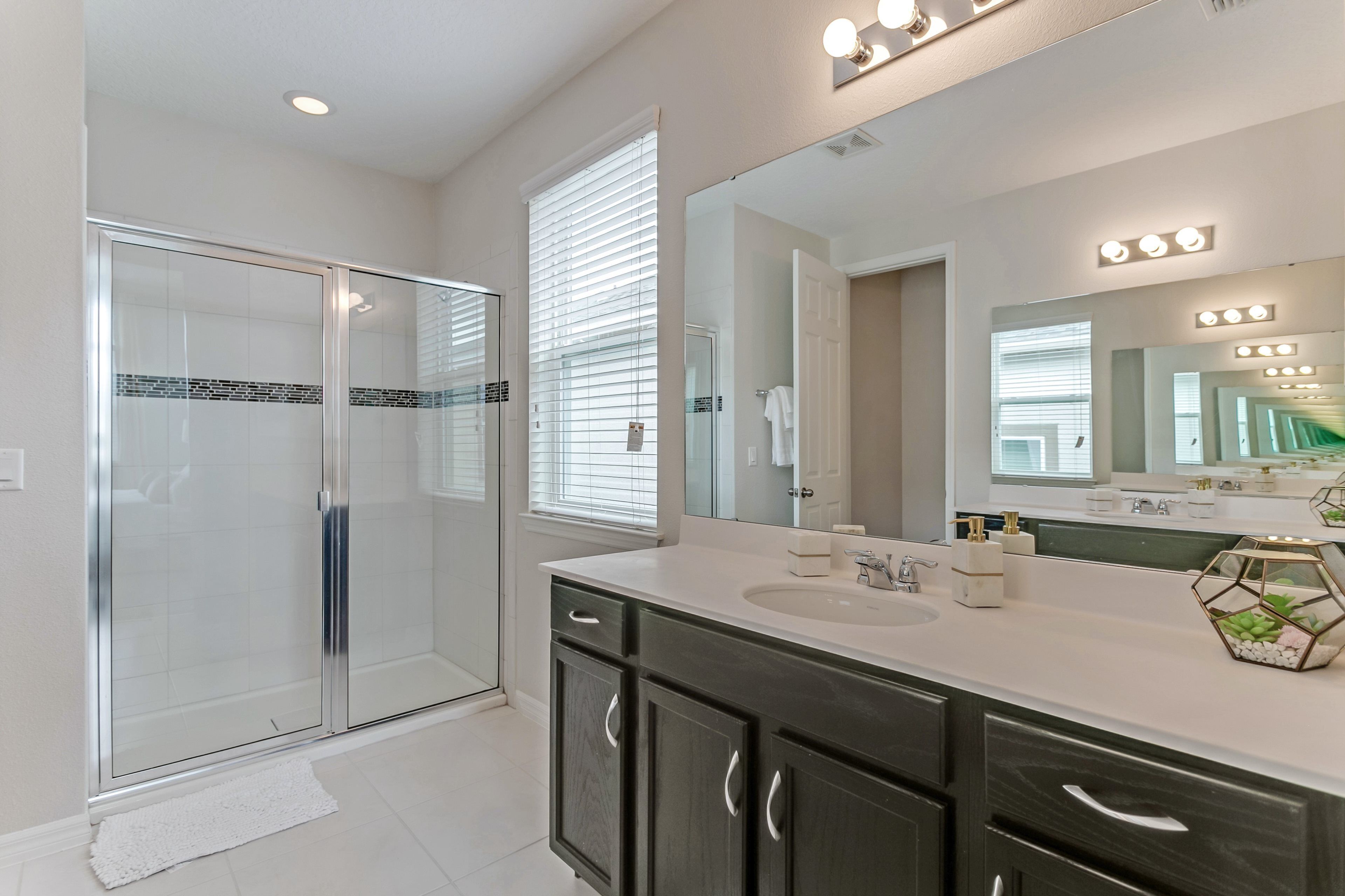 A modern bathroom with a glass shower enclosure, a large vanity with dark cabinets, and a mirror with built-in lights.