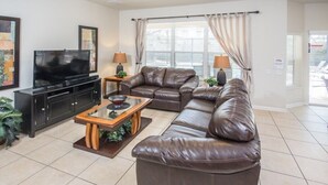 Ein Wohnzimmer mit einer braunen Ledersofa, einem Fernseher auf einem schwarzen Standfuß und einem Couchtisch mit Holzfuß.
