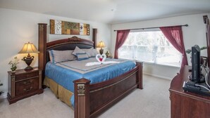 Ein Schlafzimmer mit einem großen Bett, zwei Nachttischen, einem Schreibtisch und einem Fenster mit Vorhängen.