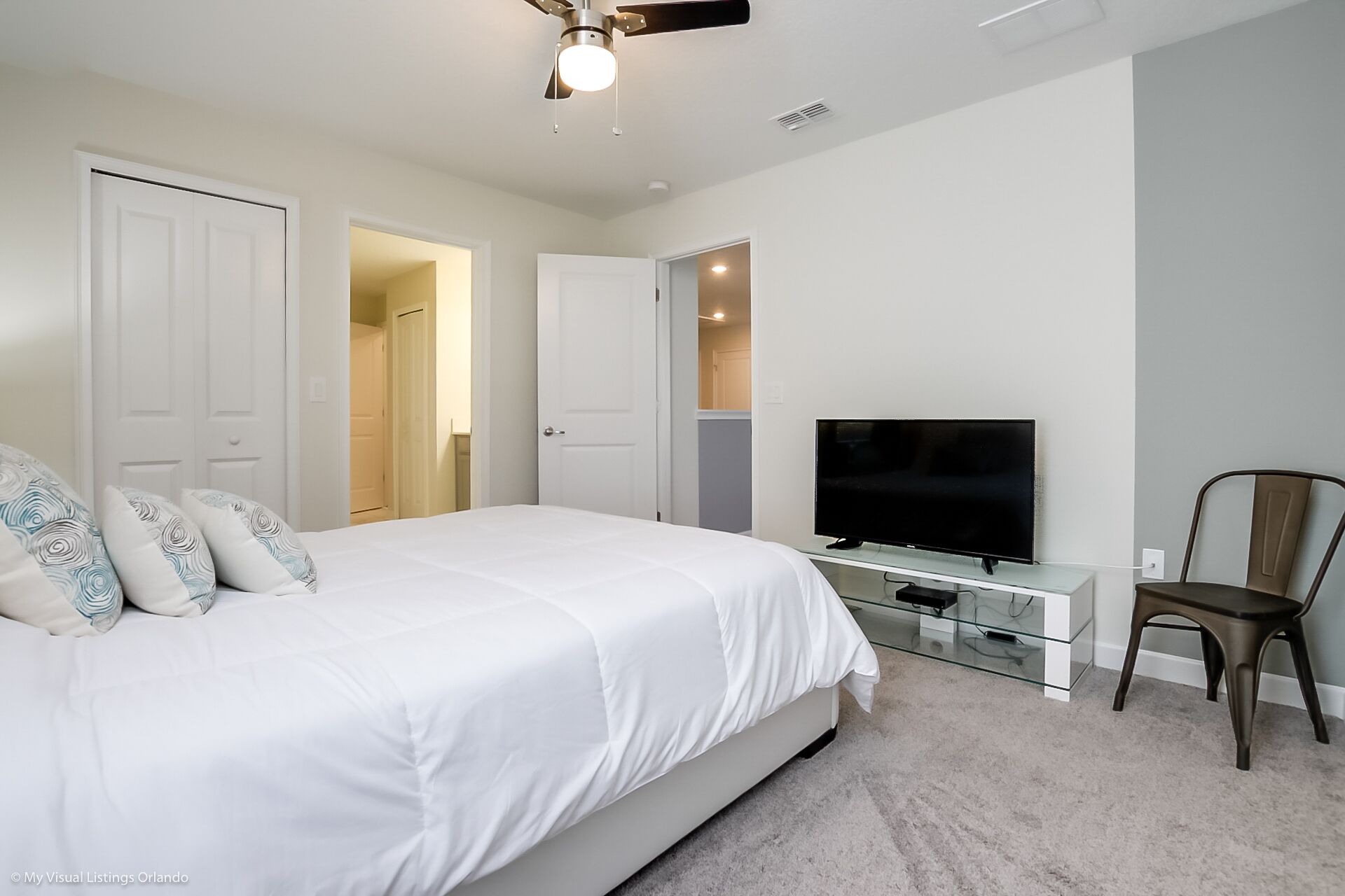 Un dormitorio con cama, televisor, sillón y ventilador de techo.