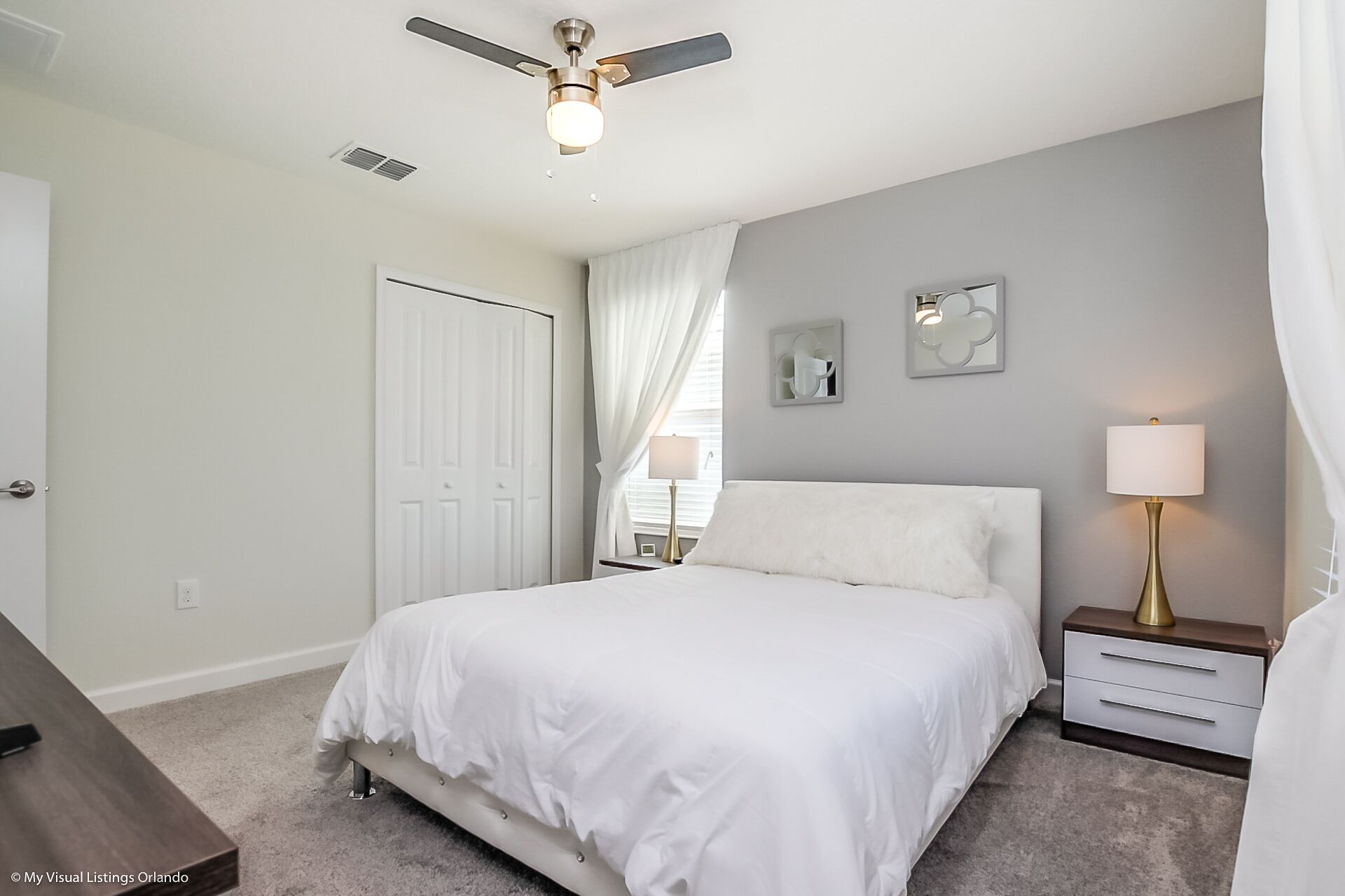 A bedroom with a bed, a nightstand, a lamp, a ceiling fan, and a door.
