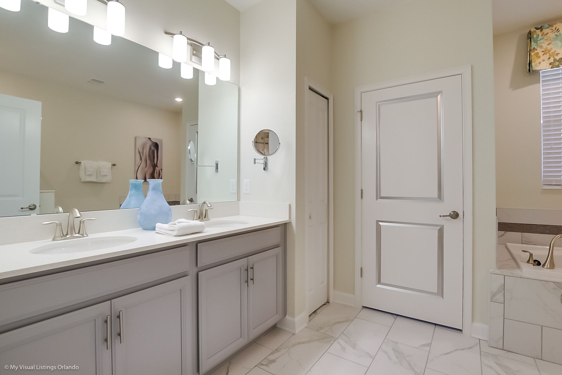 A modern bathroom with a large mirror, two sinks, and a door.