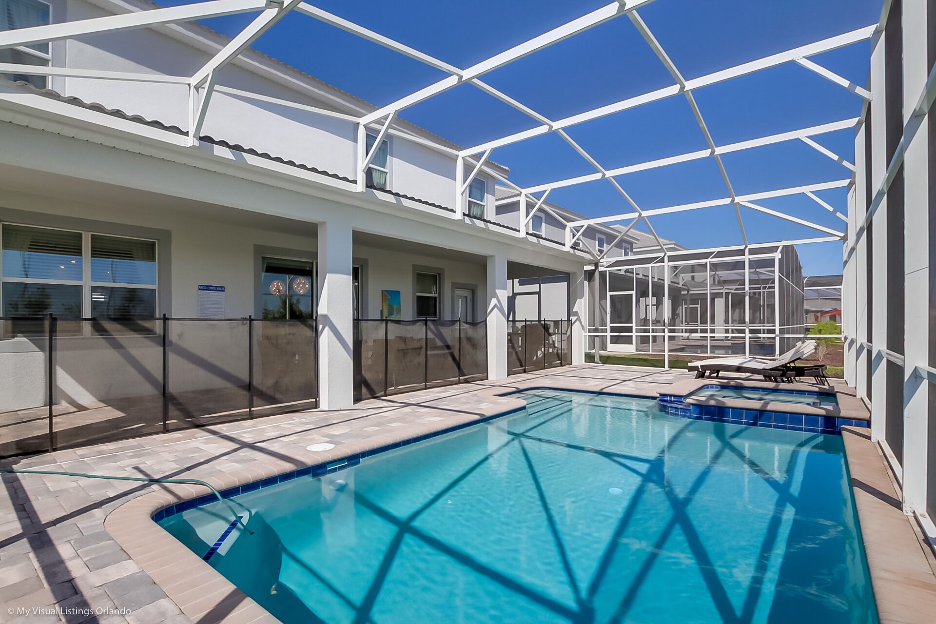 A swimming pool with a glass ceiling structure, surrounded by a white building with multiple windows and a fenced area.