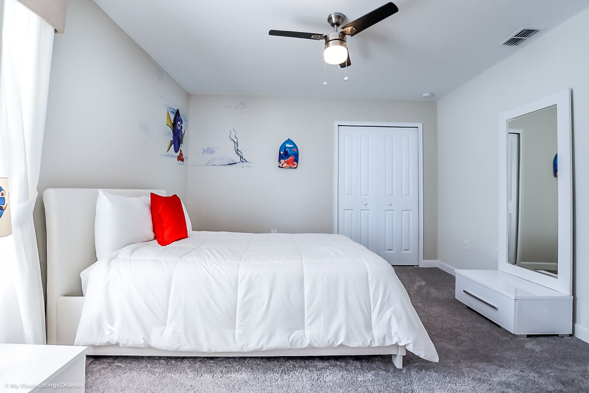 A bedroom with a bed, a ceiling fan, a wardrobe, and a large mirror.