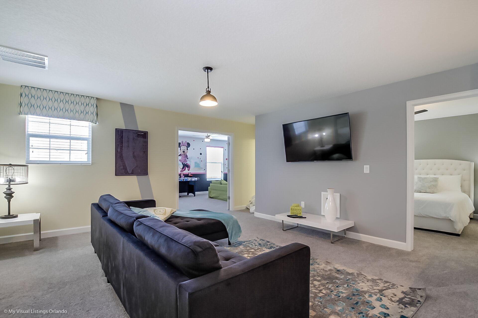 Ein modernes Wohnzimmer mit einer Couch, einem an der Wand befestigten Fernseher und einem Bett im angrenzenden Zimmer.