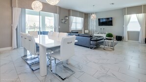 Ett modernt vardagsrum med en matplats, en grå soffa, en platt-TV och ett stort fönster med gardiner.