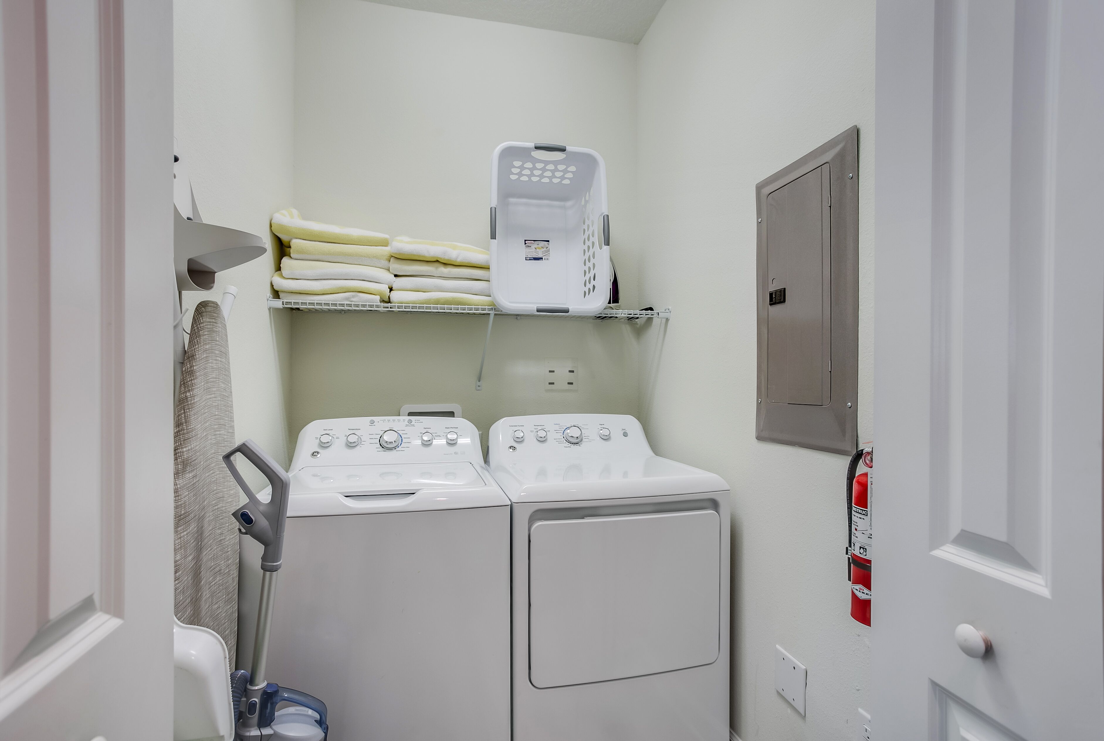 A laundry room with two washing machines, a dryer, a shelf with folded towels, and a fire extinguisher.