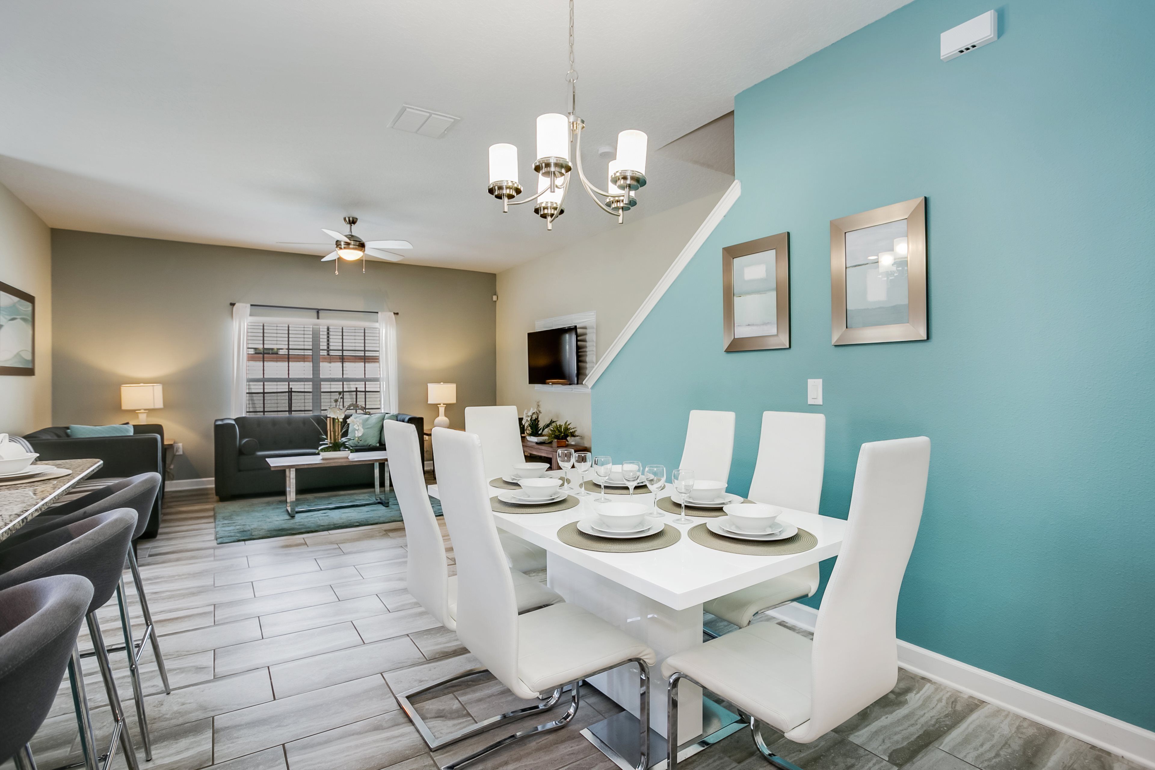 A modern dining area with a white table set for six, a ceiling fan, and a teal accent wall.