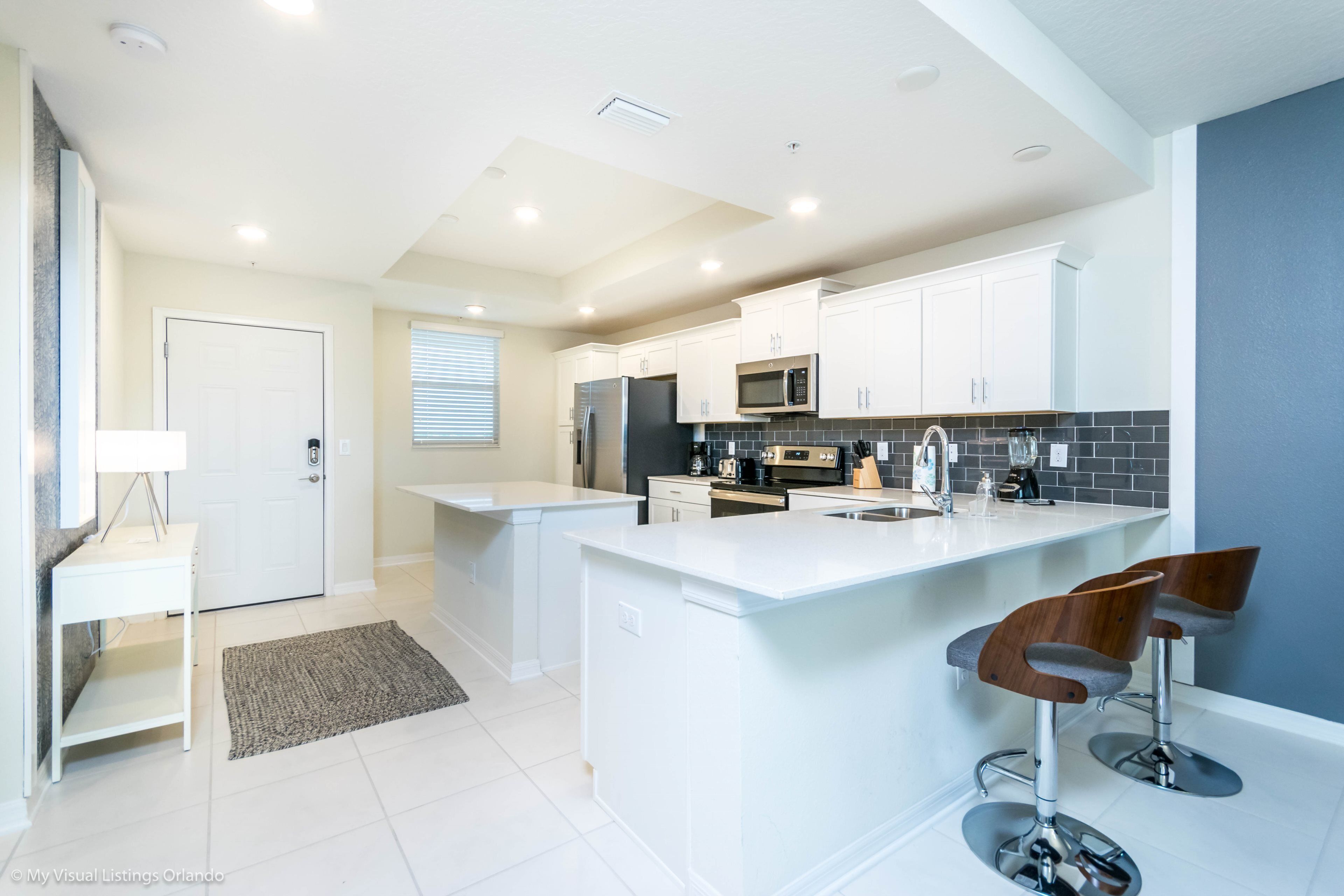 A modern kitchen with white cabinetry, a central island with bar stools, and a built-in microwave.