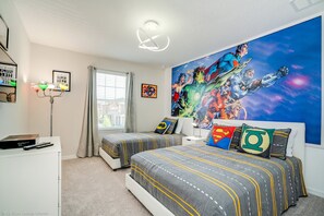 A bedroom with two beds, a large superhero-themed mural, and a desk with a lamp.