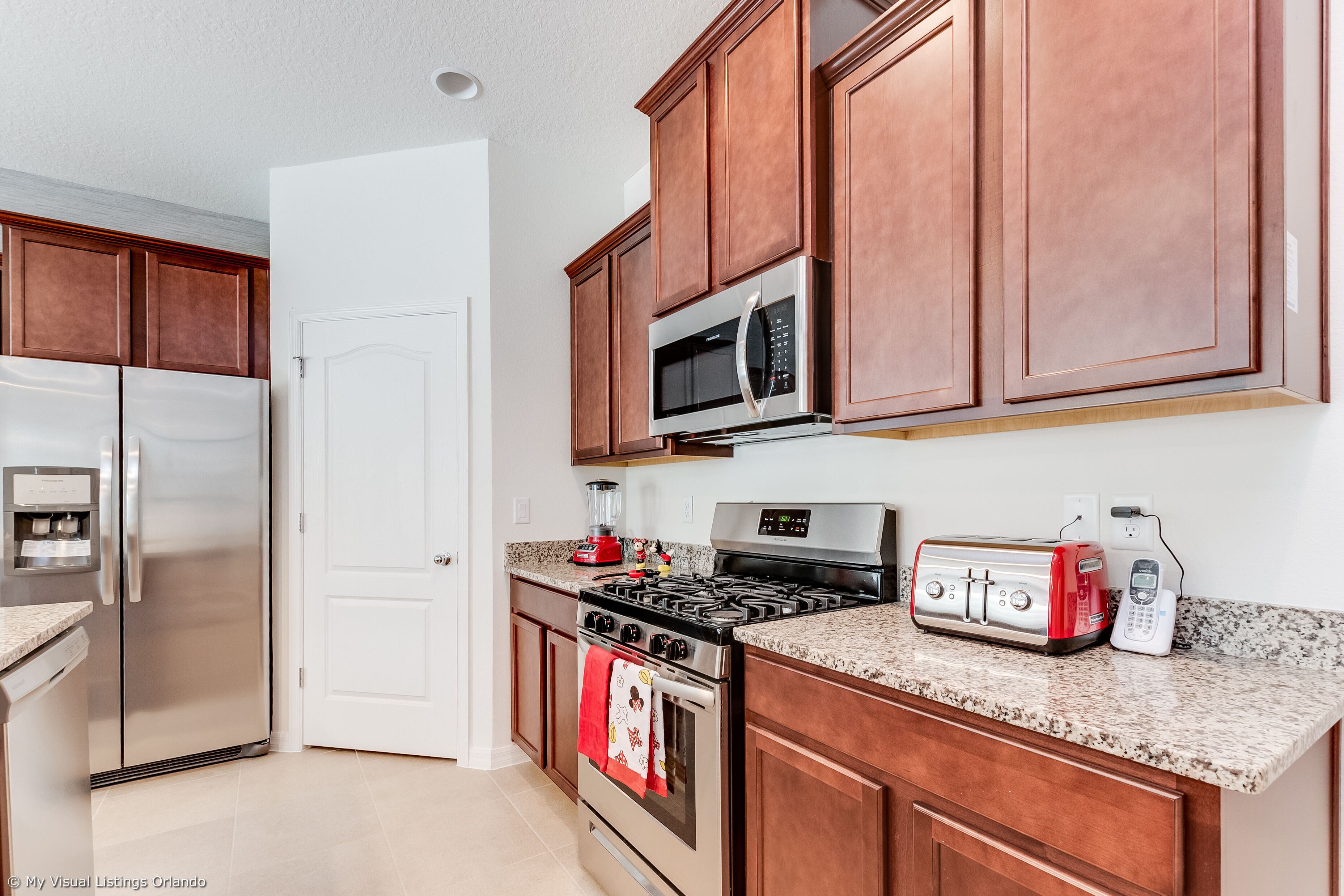 A kitchen with stainless steel appliances, wooden cabinets, granite countertops, and a red toaster.