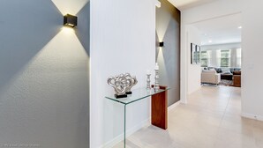 A modern hallway with a glass console table, decorative items, and wall-mounted lighting. - 5280oak Luxury Ne 6 Bedroom 4.bath Home (Davenport)