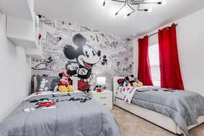 A bedroom with two beds, a Mickey Mouse mural on the wall, and red curtains.