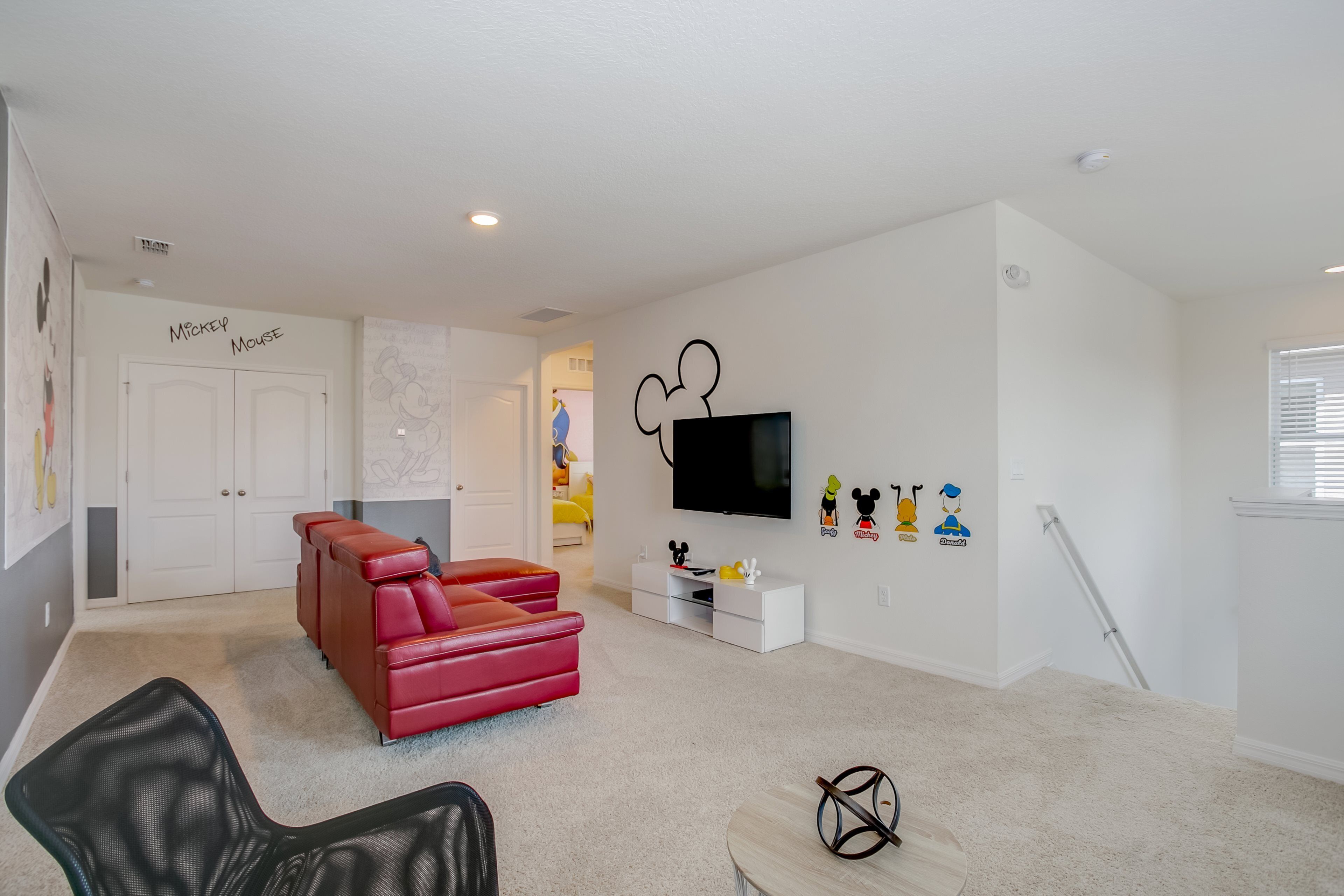 A modern living room with a red sofa, a flat-screen TV, and Mickey Mouse decorations.