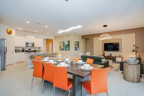 A modern kitchen with white cabinets, a dining area with orange chairs, and a living room with a sofa and a TV. - 5 Bedroom 5 Bath Villa (Davenport)