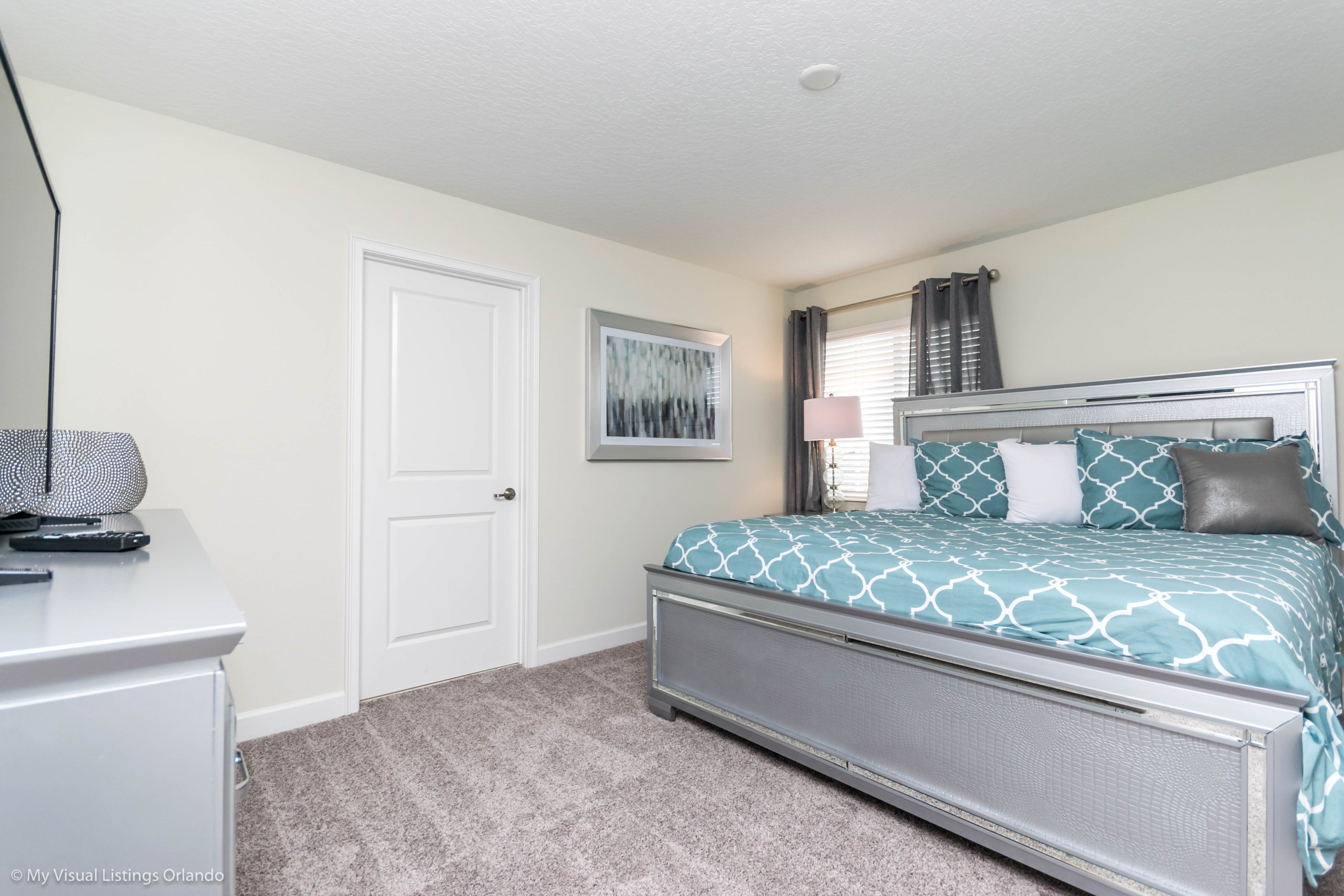 A bedroom with a bed, a desk, a door, and a window with curtains.