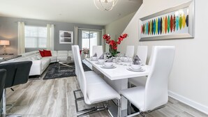 Un espace repas moderne avec une table blanche dressée pour six personnes, entourée de chaises blanches.