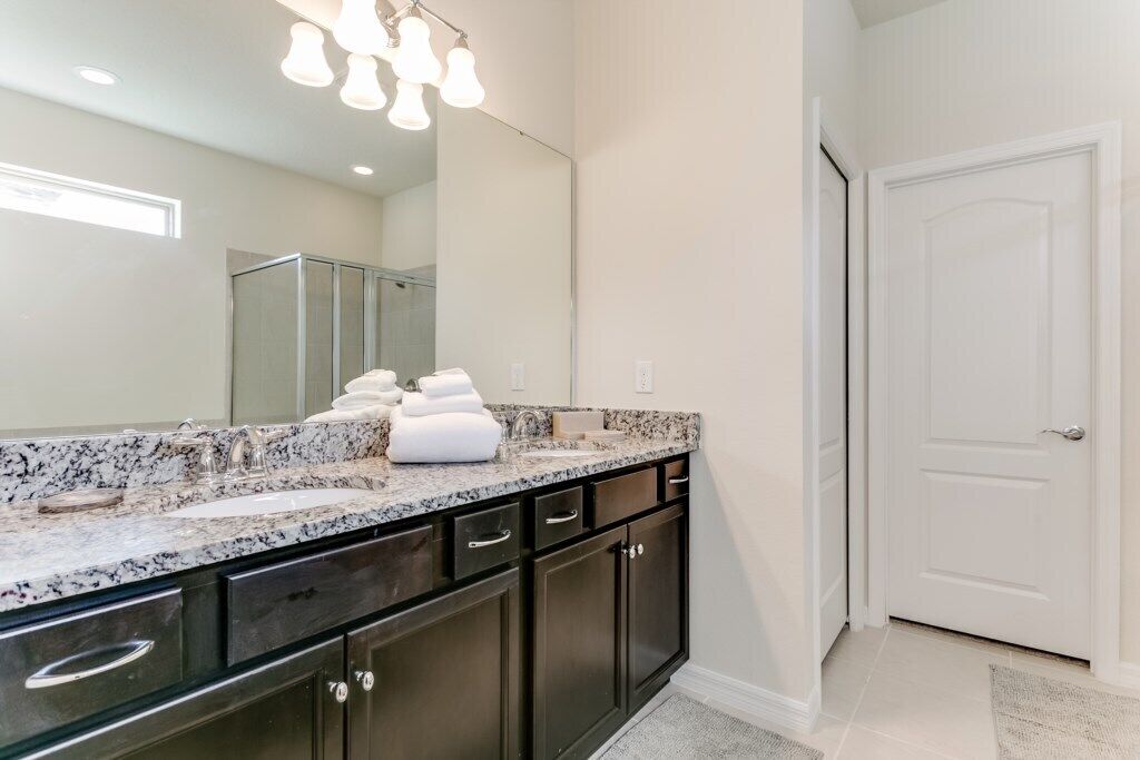 A modern bathroom with a granite countertop, dark cabinets, and a large mirror.